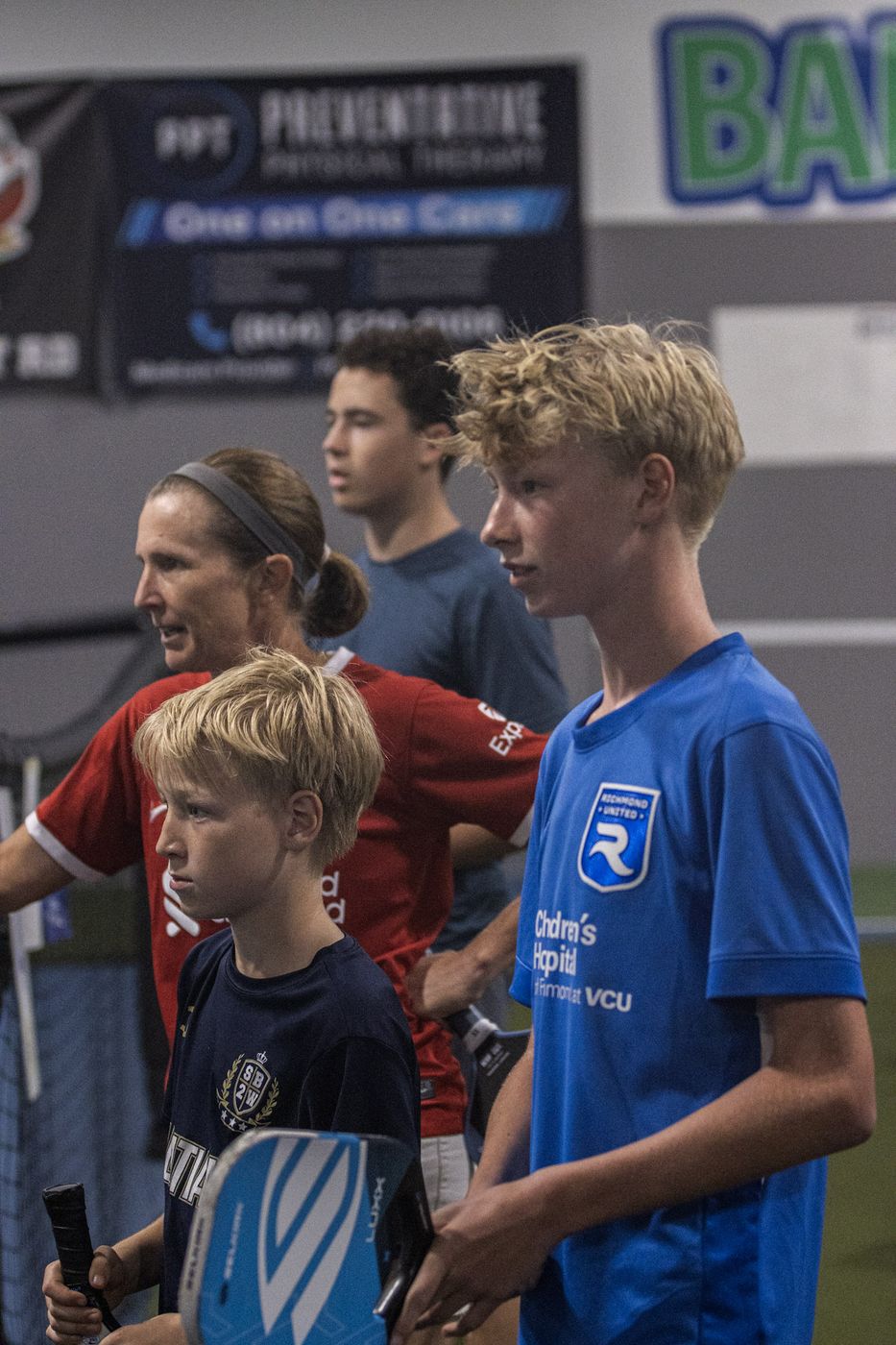 Young players waiting courtside with their paddles